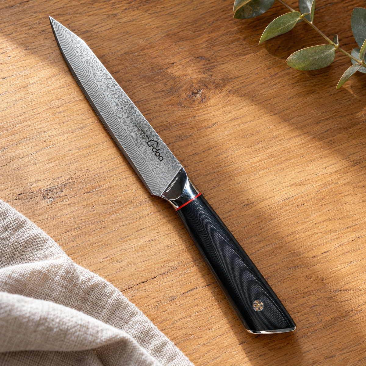 i-DOO 5-inch black-handle Damascus utility knife on warm oak with linen and eucalyptus